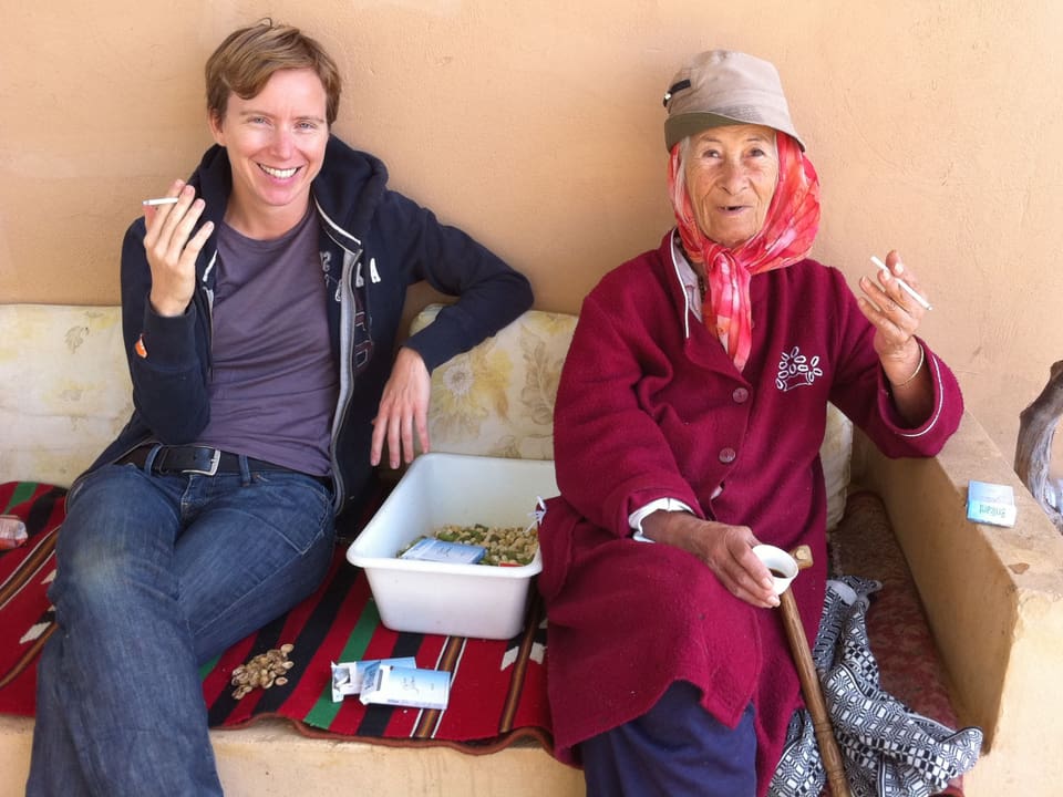 Die Radiojournalistin Christina Caprez und die 80-Jährige Nabiha sitzen zusammen auf einer Bank und rauchen. 