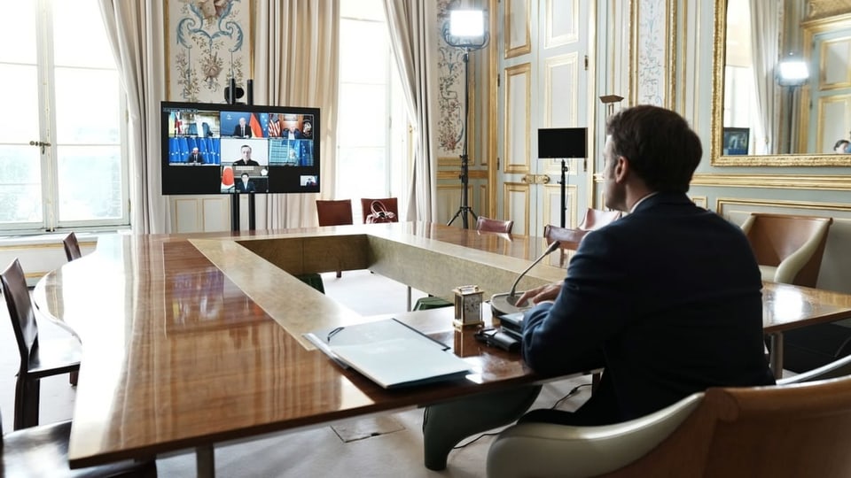Emmanuel Macron an langem Tisch mit TV am anderen Ende