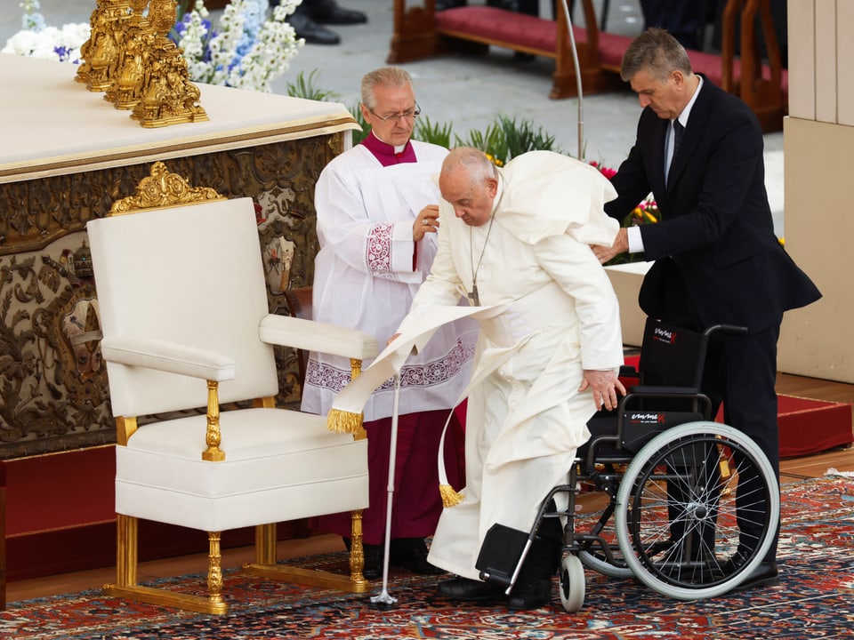 Der Papst im weissen Ornat steht vom Rollstuhl auf.