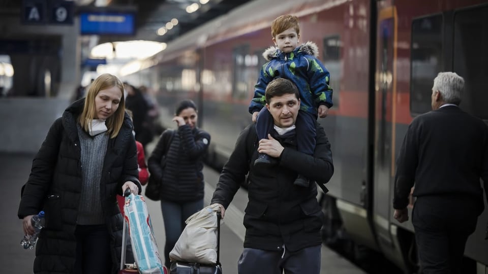 Mutter, Vater und Kind kommen mit Gepäck an einem Schweizer Bahnhof an.