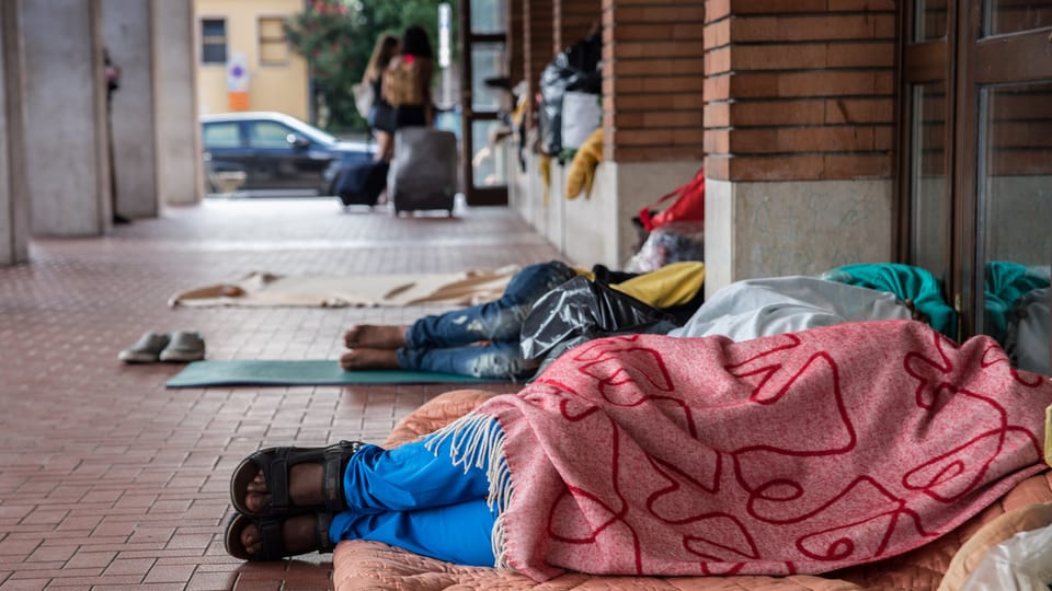 Migranten liegen in Decken gehüllt vor dem Bahnhofsgebäude in Como.