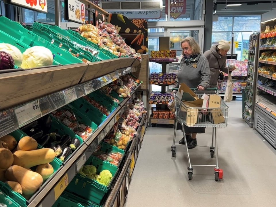 Eine Frau steht vor einer Gemüseauslage in einem britischen Supermarkt.