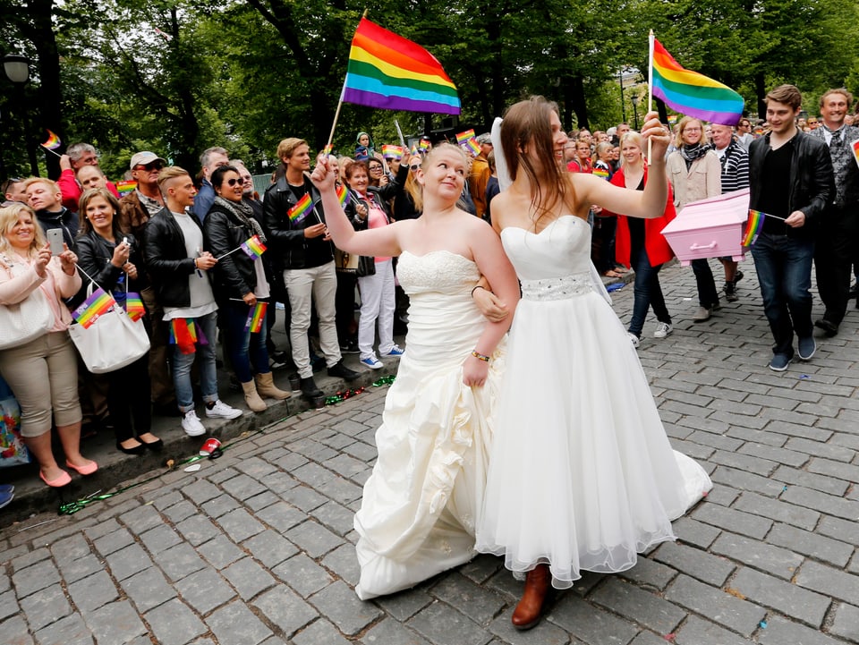 Lesbisches Paar in Brautkleidern und Regenbogenfahne