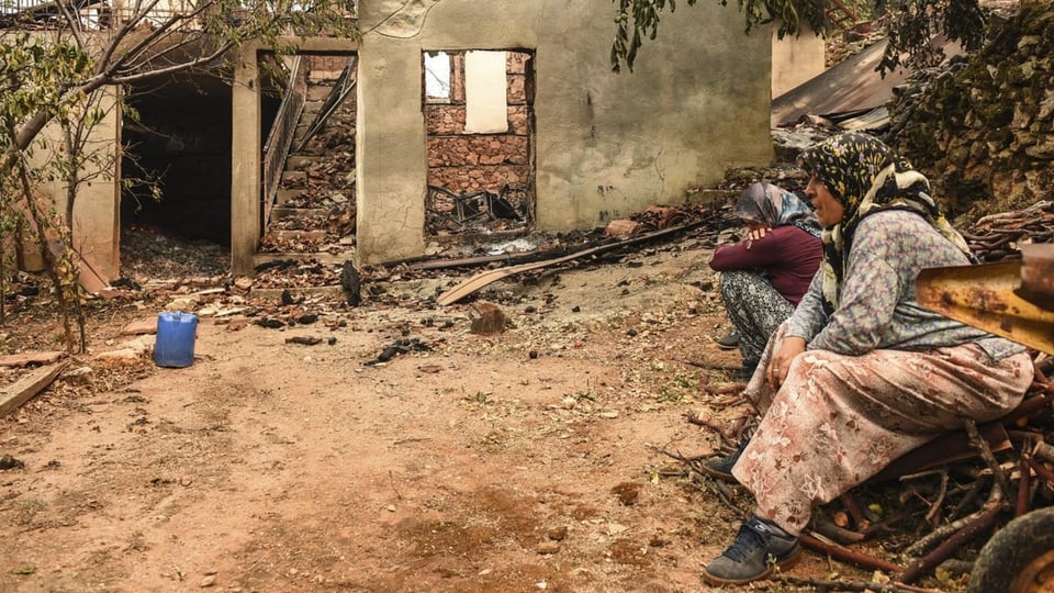 Zwei Frauen sitzen vor ihrem abgebrannten Haus.