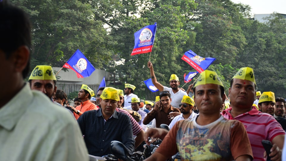 Männer mit gelben Käpchen und Flaggen protestieren.