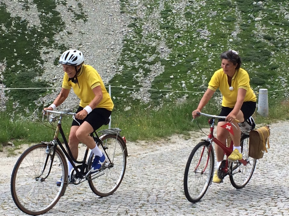 Anna und Marlies sitzen auf dem Fahrrad und fahren die gepflästerte Strasse am Gotthard hoch.