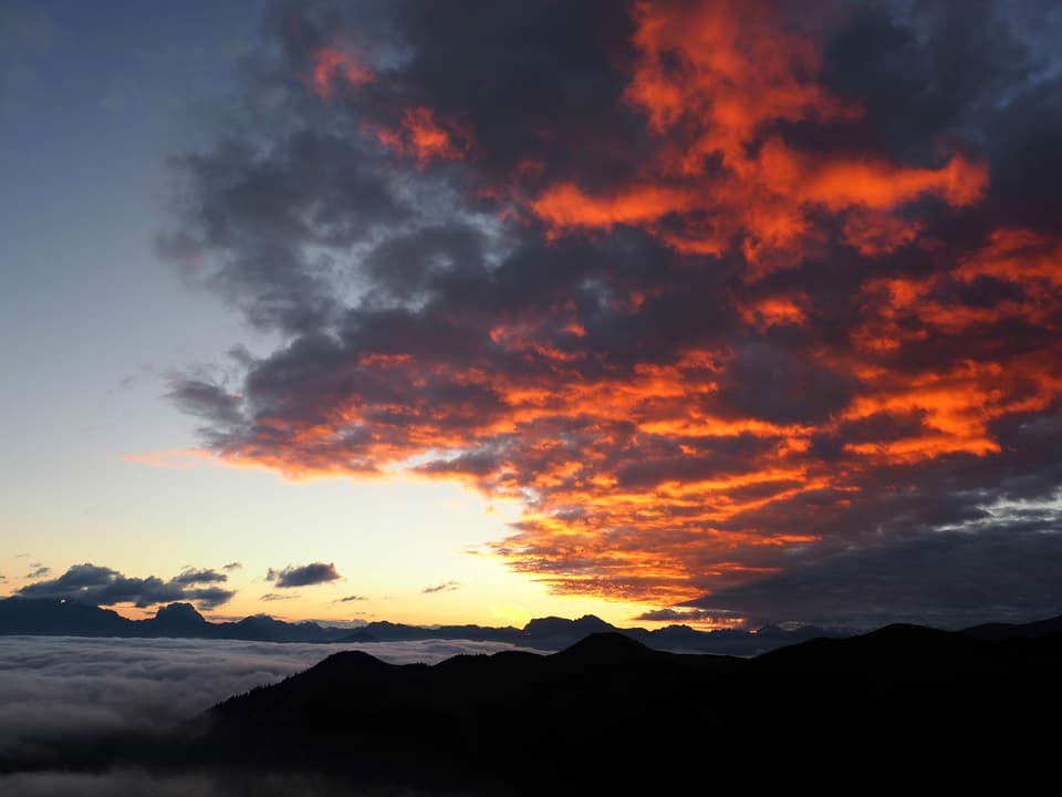 Die Sonne lässt Wolkenfelder rot erscheinen. Blick von Berg, im Tal Hochnebel.