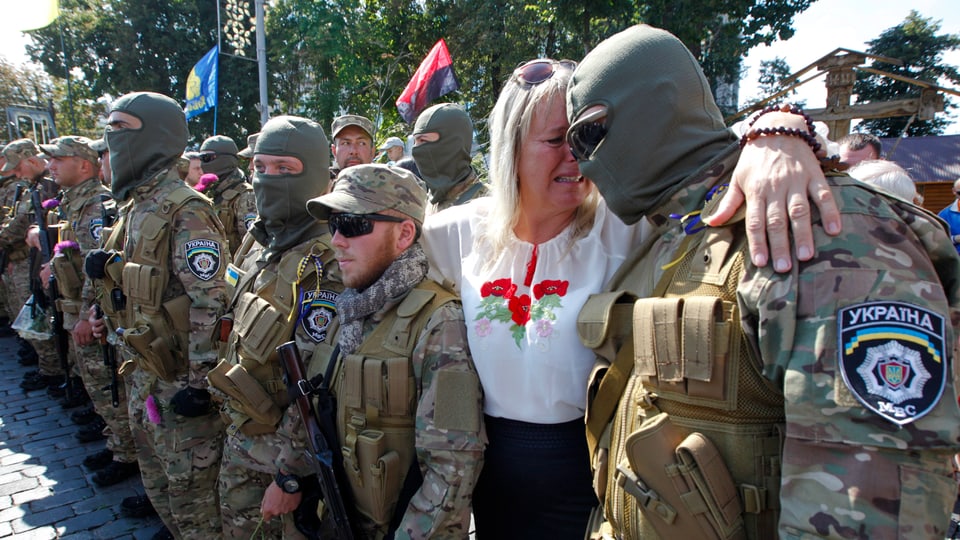 Soldaten stehen in einer Reihe, neben einem steht eine weinende Frau, seine Mutter.