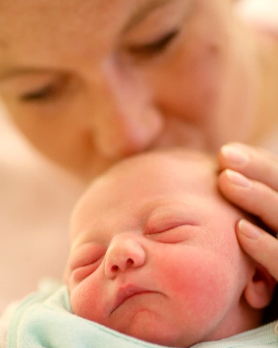Ein Baby wird sanft von seiner Mutter am Kopf gestreichelt.