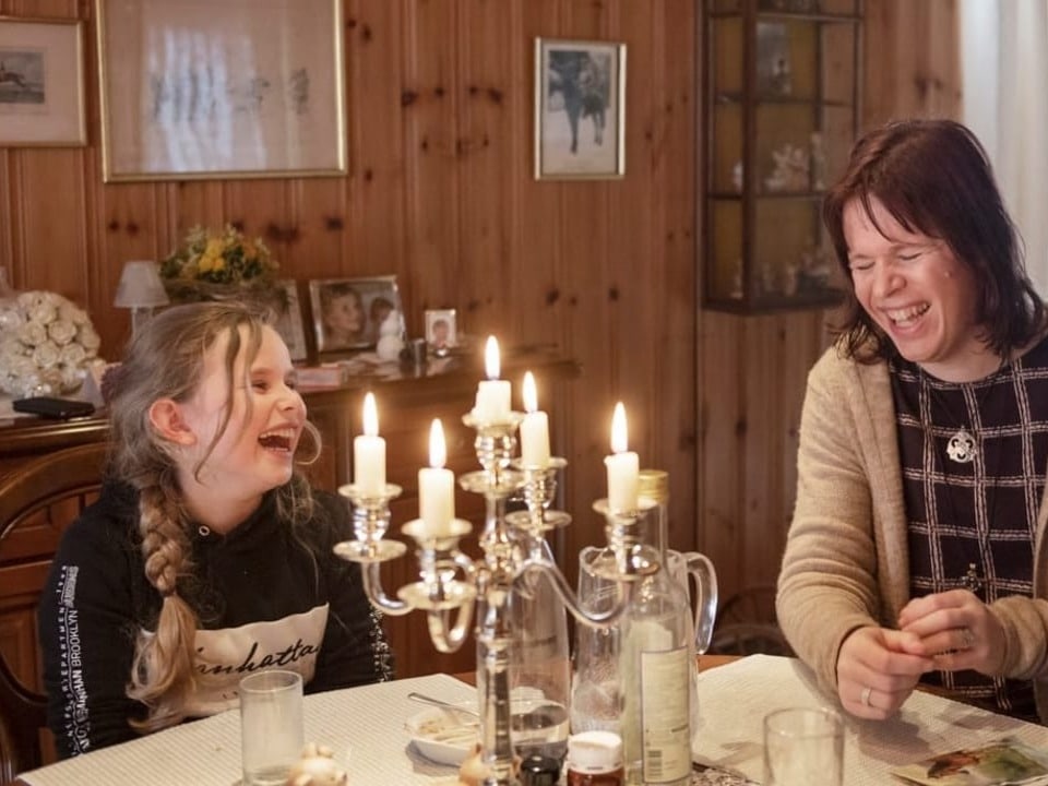 ein junges Mädchen und eine Frau sitzen am Küchentisch und lachen