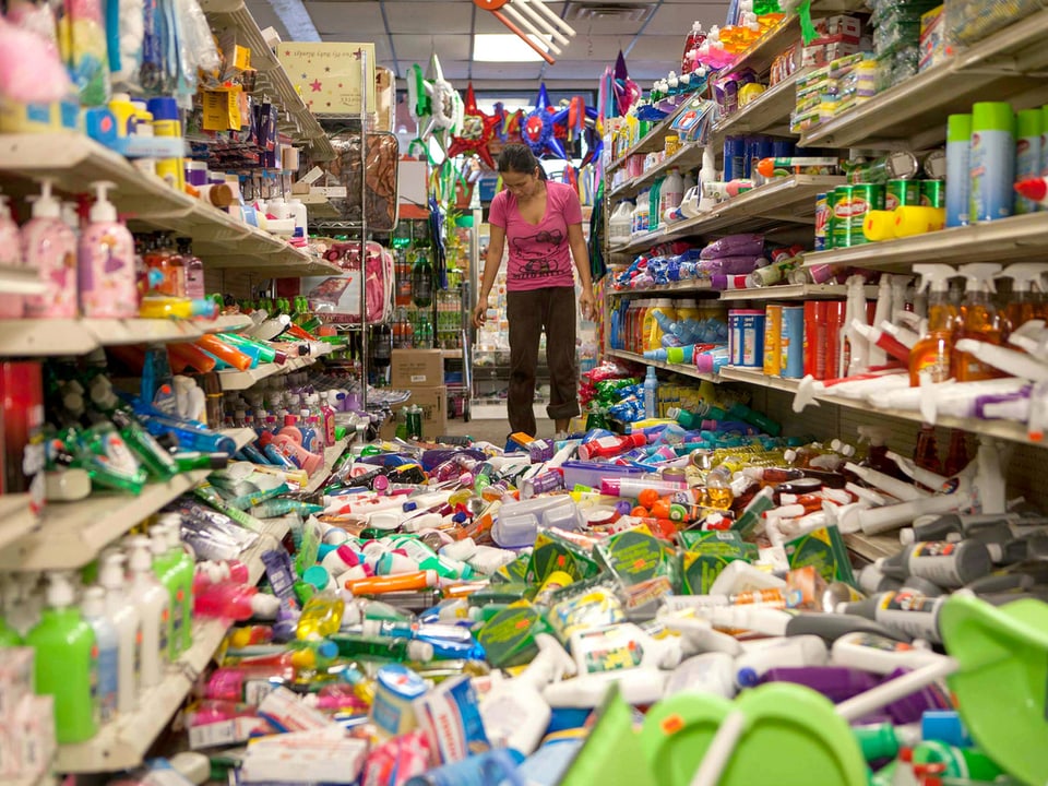 In einem Geschäft liegen bunte Plastikflaschen am Boden, dahinter steht eine Frau und sieht auf den Boden