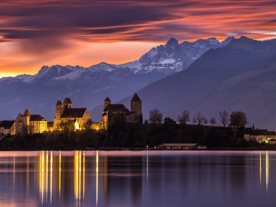 Rapperswil/SG Blick über den See auf Altstadt, im Hintergrund Alpen mit rot leuchtenden Wolken.