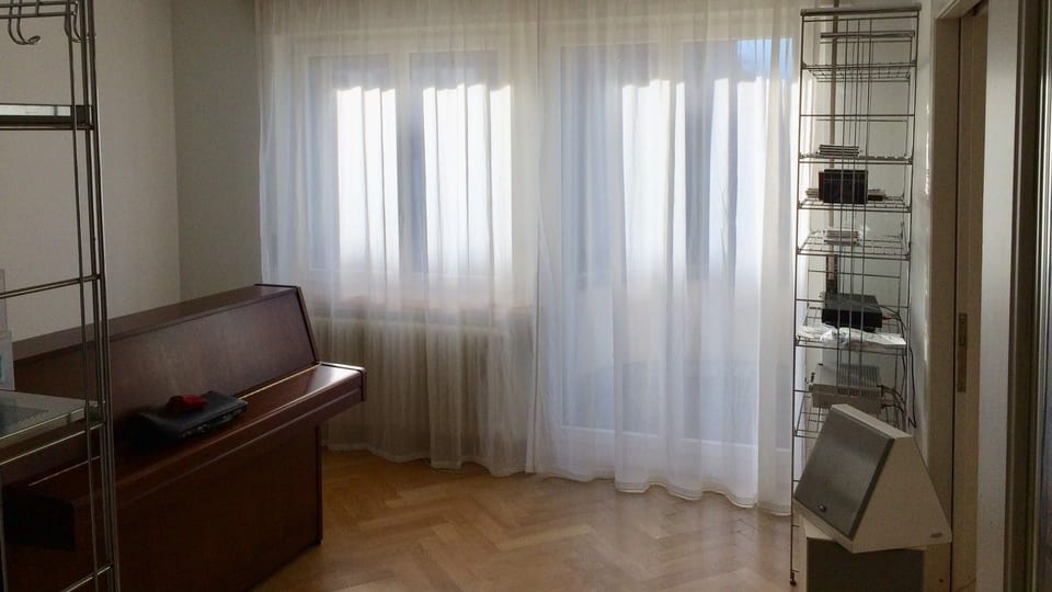 Wohnung innen, Parkettboden, Klavier, Fenster mit Vorhang.