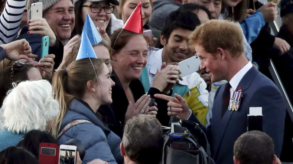 Prinz Harry geht auf eine Gruppe Frauen mit Party-Hüten zu und zeigt mit dem Finger auf diese.