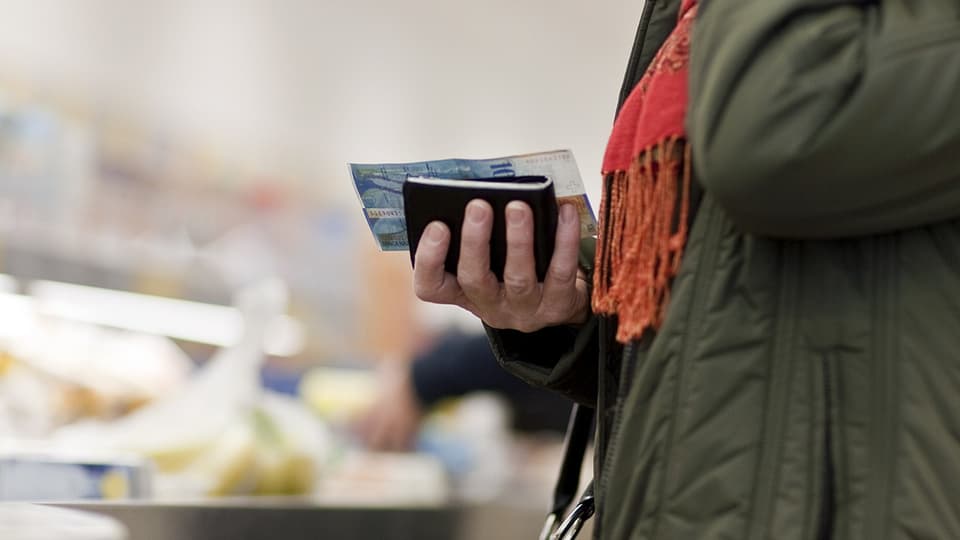 Eine Frau hält eine 100er-Note und ihr Portemonnaie in der Hand. 