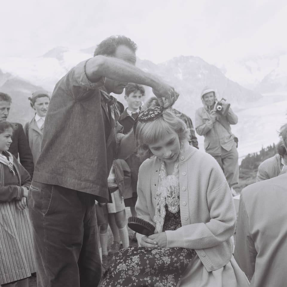 Ein Maskenbildner rückt die Frisur von Nelly Borgeaud zurecht. Borgeaud hält einen Kamm in der Hand.