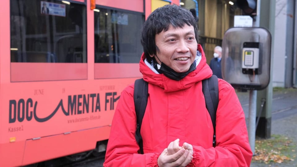 Ein Mann mit roter Jacke steht vor einer Strassenbahn.