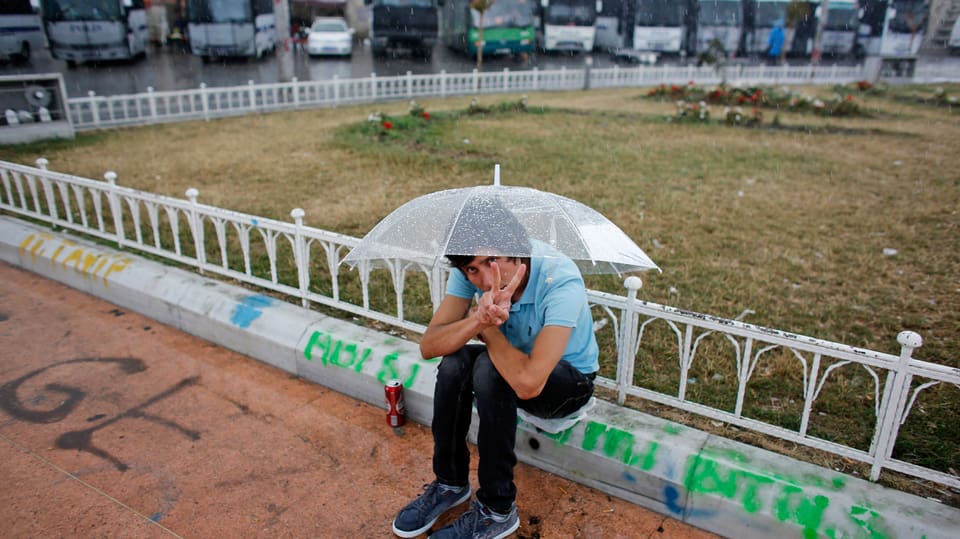 Ein junger Demonstrant unter einem Regenschirm macht mit den Fingern ein Siegeszeichen.