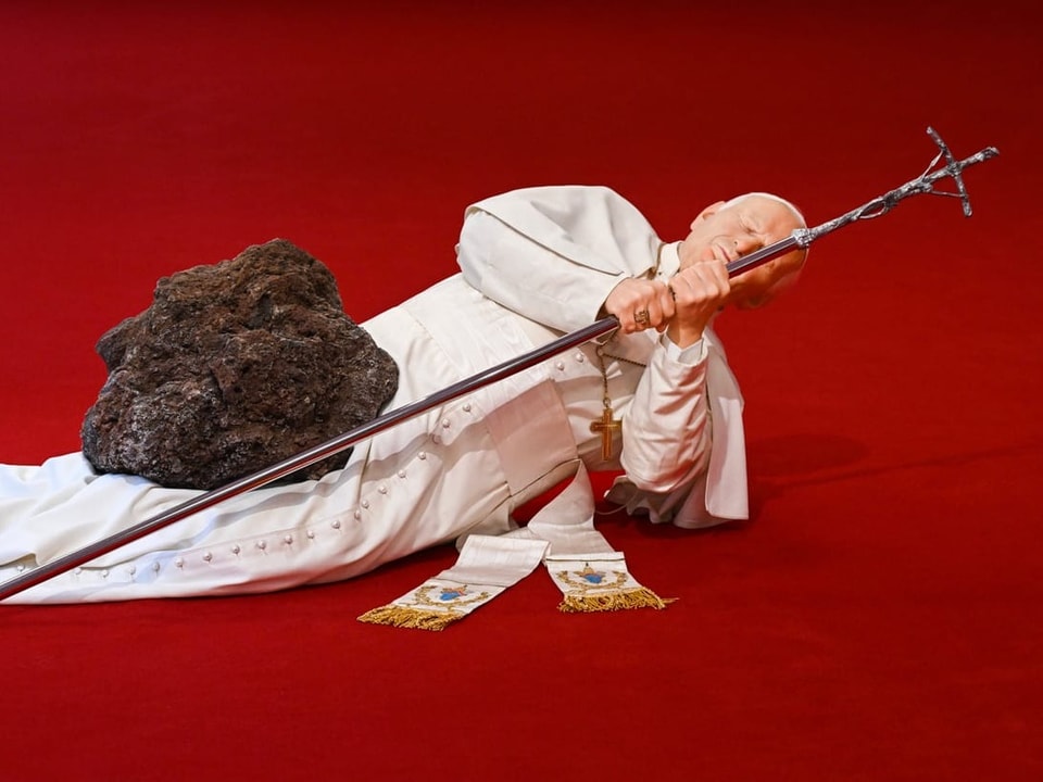 Papst-Figur, die von einem Meteoriten getroffen wird liegt am Boden