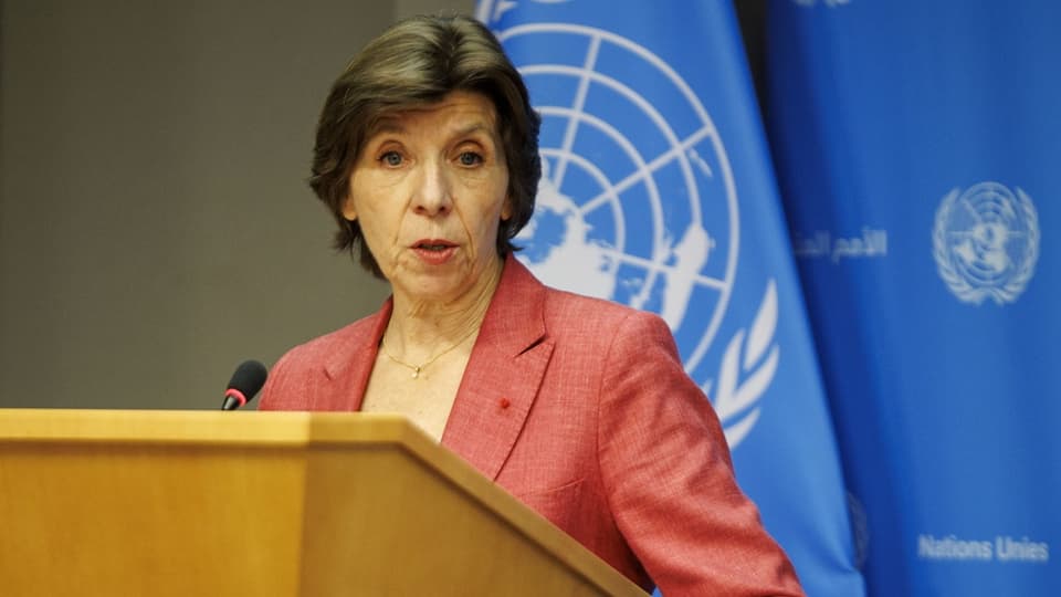 Catherine Colonna steht hinter einem Mikrofon und vor einer Flagge mit dem Logo der Vereinten Nationen.