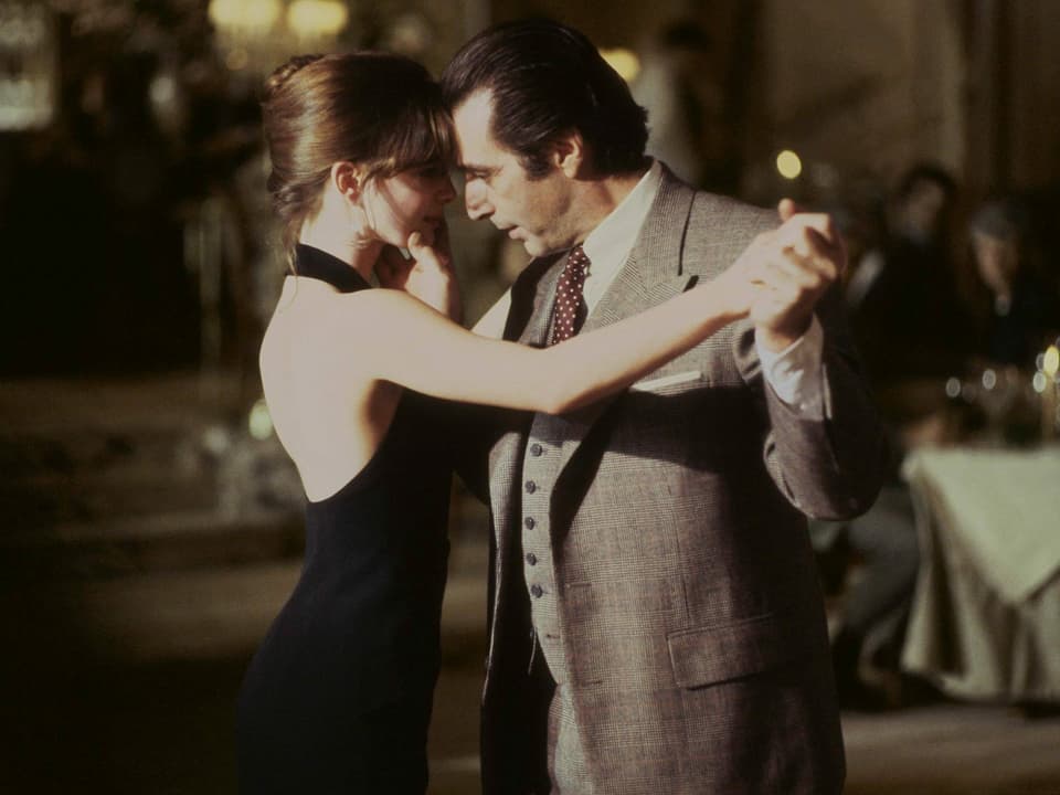 Al Pacino als Frank Slade im Film "Der Duft der Frauen". Er tanzt mit einer jungen Frau. Sie trägt ein schwarzes, rückenfreies Kleid. Die beiden tanzen nah beieinander. Er hält dabei ihr Gesicht mit der Hand.