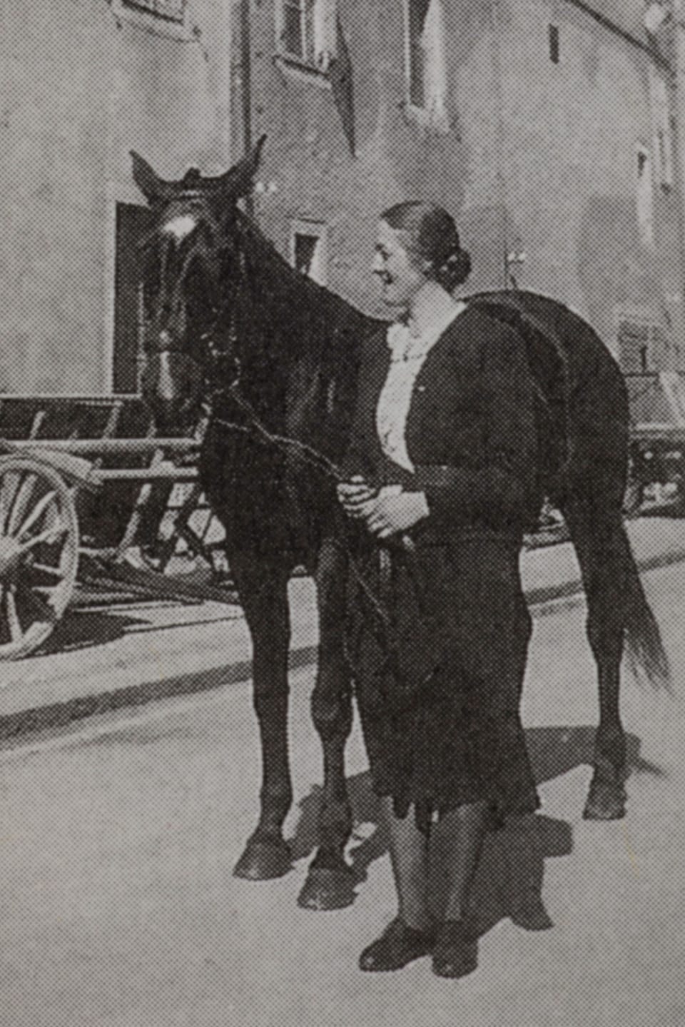 Eine Frau und ein Pferd stehen auf einer Strasse.