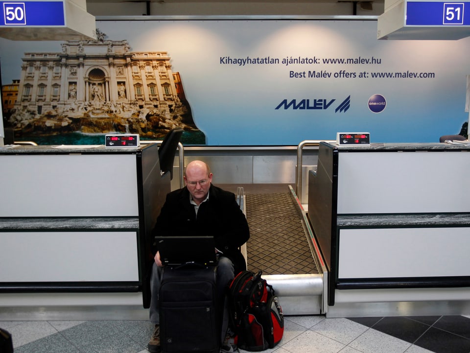 Reisender sitzt auf dem Rollband am Malev-Check In und arbeitet mit seinem Laptop.