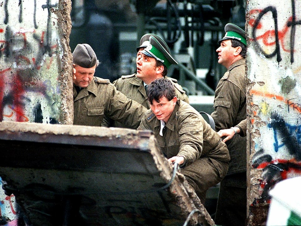 Ostdeutsche Grenzsoldaten helfen beim Einreissen eines Stücks der Berliner Mauer.