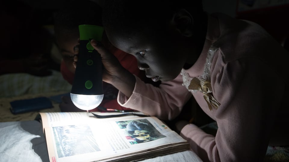 Kind mit Taschenlampe über einem Schulbuch