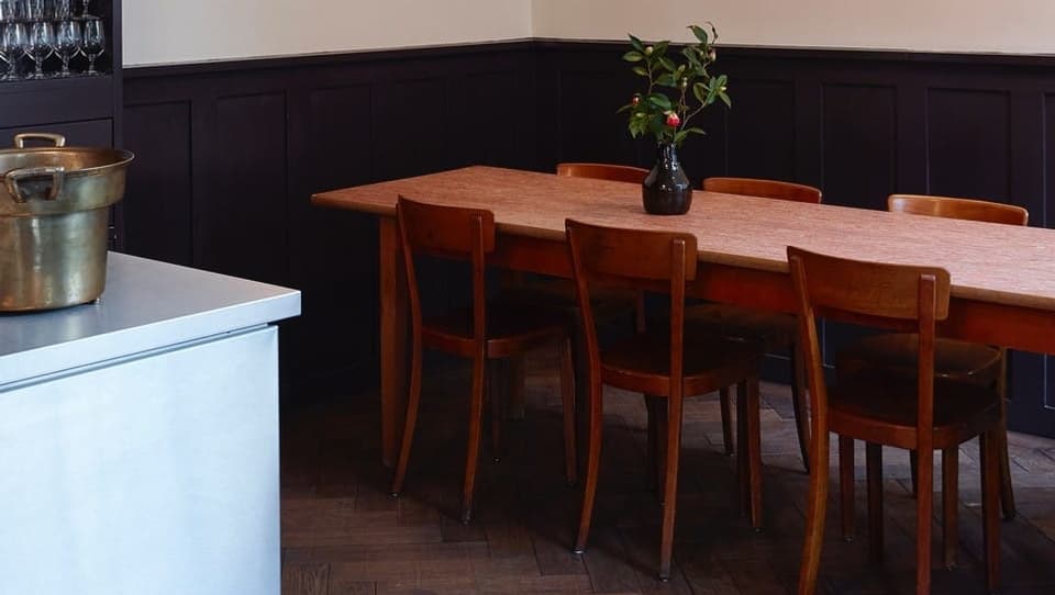 Blick auf einen langen, ungedeckten Holztisch mit einer Blumvase drauf im Restaurant Gamper.