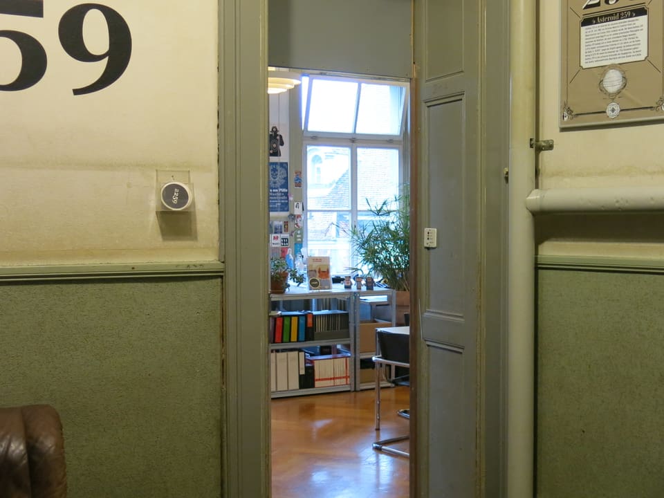 Blick durch eine offene Türe auf ein Büchergestell und einen Stuhl.