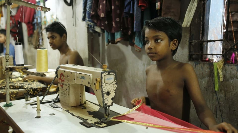 Junge Kinder arbeiten an Nähmaschinen in einem engen, schlecht beleuchteten Raum.