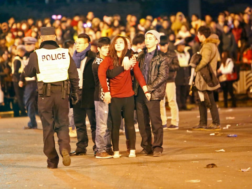 Drei junge Männer und eine junge Frau stehen fassungslos mitten auf einem von der Polizei abgeriegelten Platz.