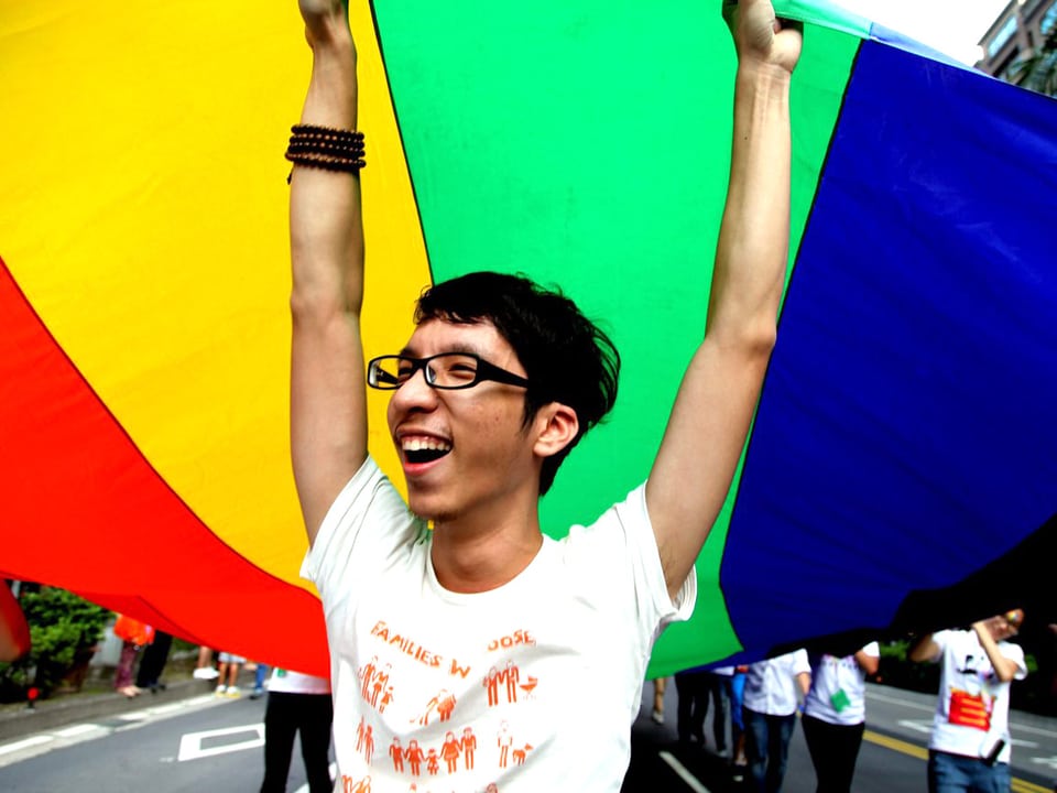 Ein junger Mann hält den Anfang einer meterlangen regenbogenfarbenen Fahne in die Luft.