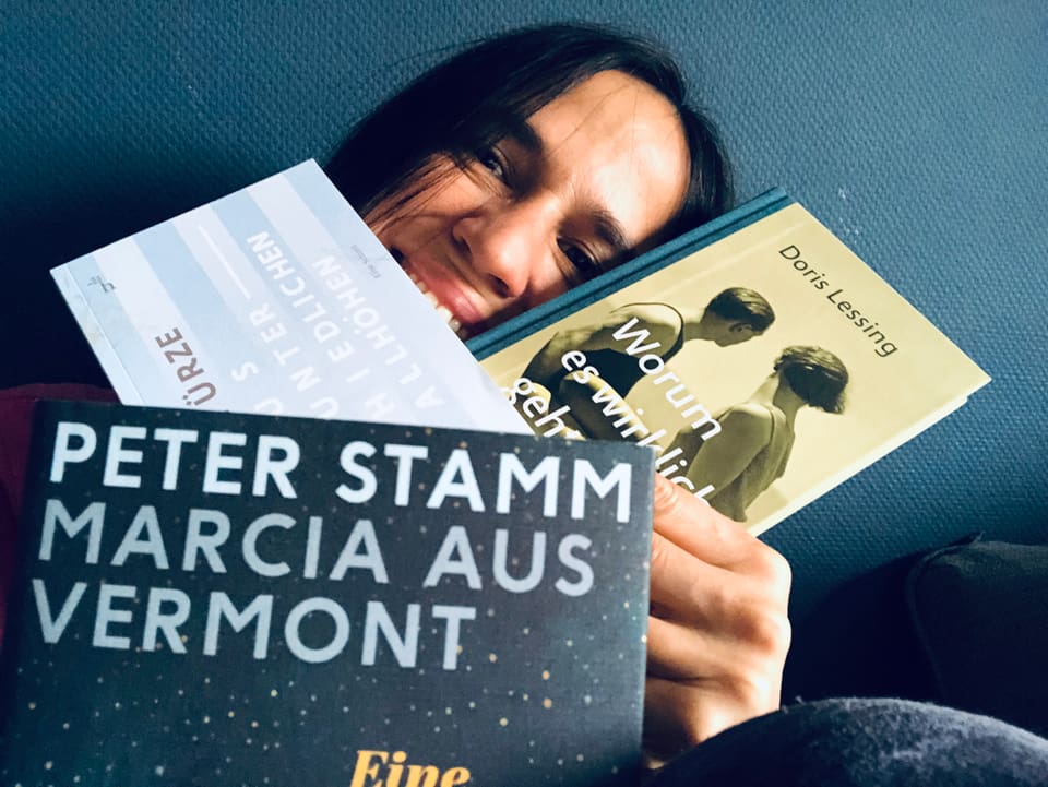 Annette König vor einer blauen Tabetenwand mit drei Sammelbänden mit Short Stories.