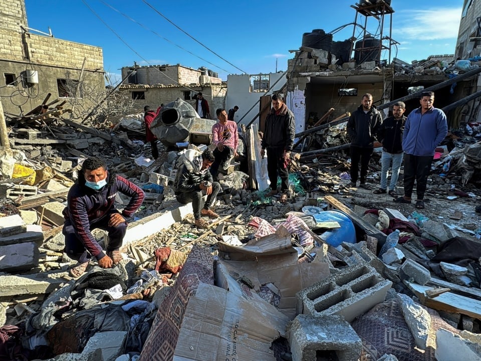 Männer gehen auf Trümmern eines zerstörten Gebäudes