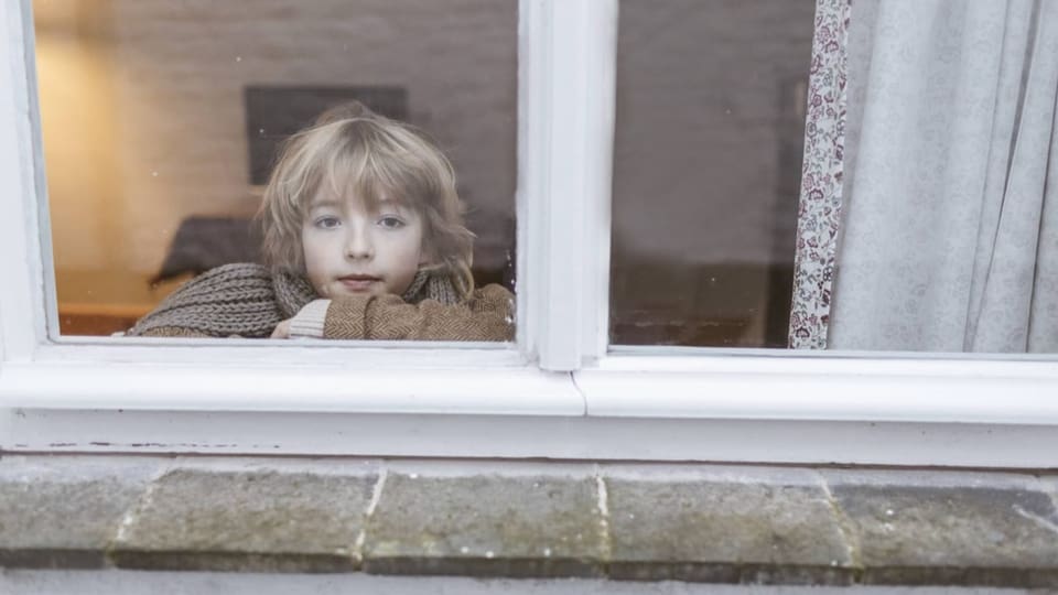 Eine Junge schaut aus dem Fenster.