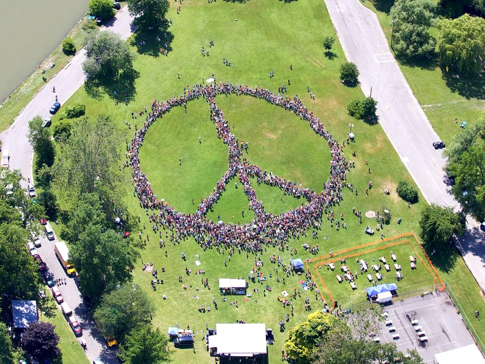 Menschen in einem Park formieren sich zu einem riesigen Peace-Zeichen.