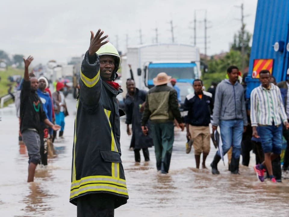 Feuerwehrmann dirigiert Menschen durch überflutete Strasse