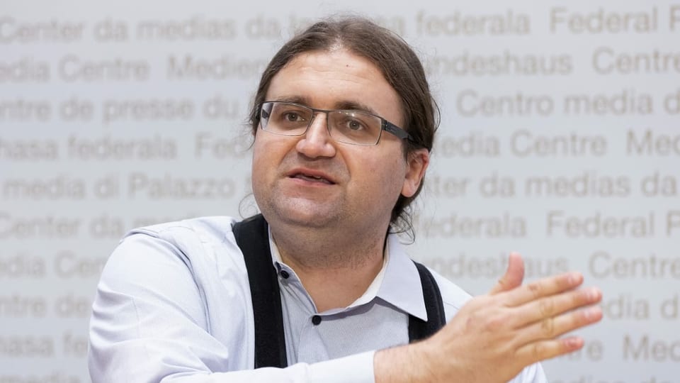 Jörg Mäder trägt eine Brille und hat lange Haare, die er hinten zusammengebunden hat. Bild von einer Pressekonferenz im Dezember 2020.