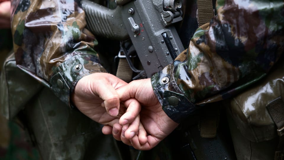 Hände eines Soldaten, der sie hinter seinem Rücken hält. Darunter ist seine Waffe.