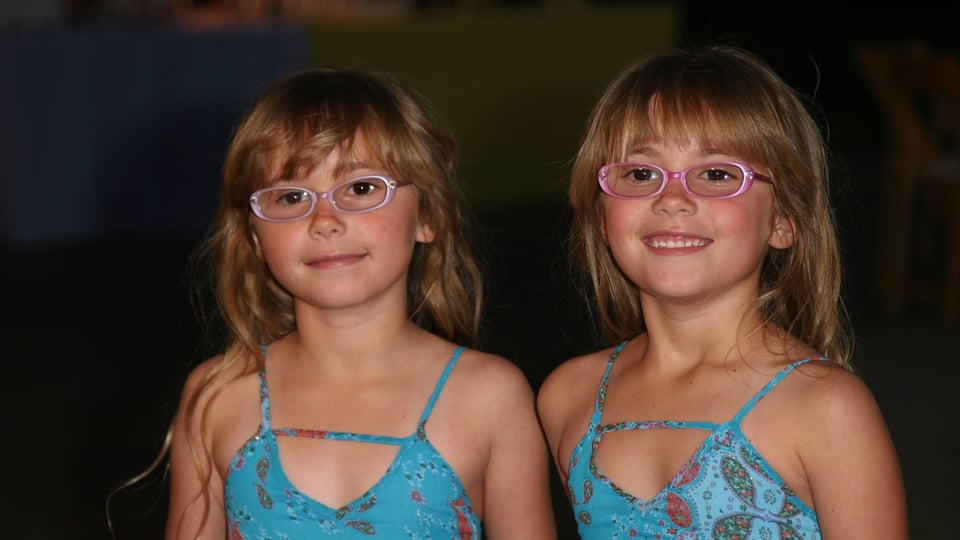 Eineiige Zwillingsmädchen tragen ihre Brillen.