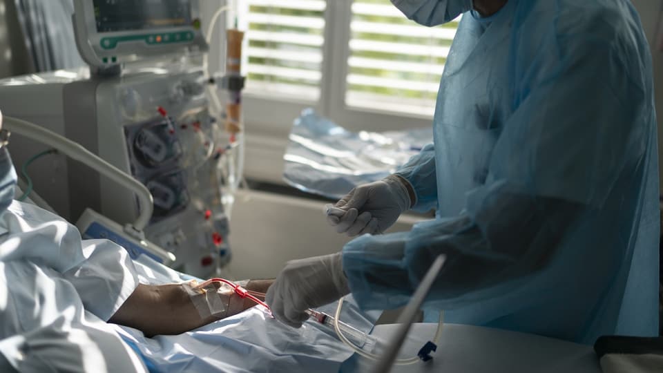 Ein Pfleger steckt die Nadel in den Arm eines Patienten, um ihn an das Dialysegerät anzuschliessen.