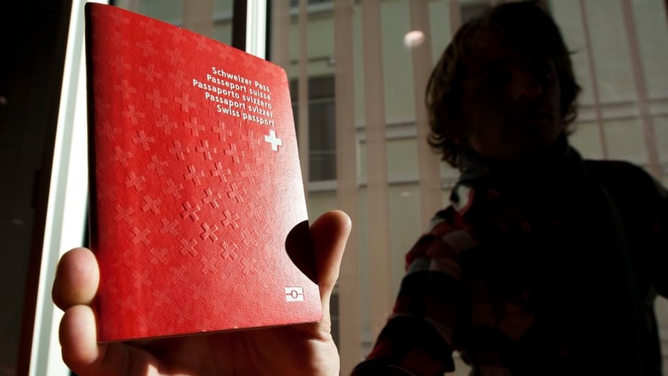 Eine unbekannte Person hält eine Schweizer Pass in die Kamera.