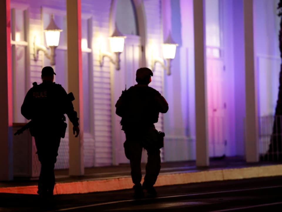 Zwei schwer bewaffnete Sicherheitskräfte patrouillieren vor einer violett erleuchteten Fassade des Casino Tropicana in Las Vegas.