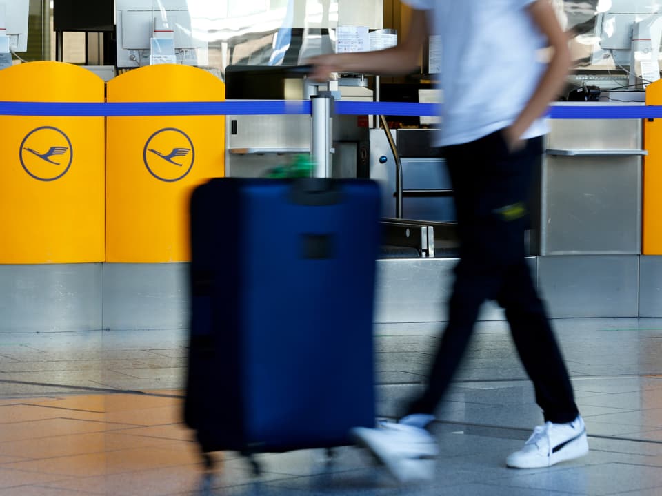 Ein Mann läuft mit einem Koffer durch einen Flughafen. Im Hintergrund sind Lufthansa-Logos zu sehen.