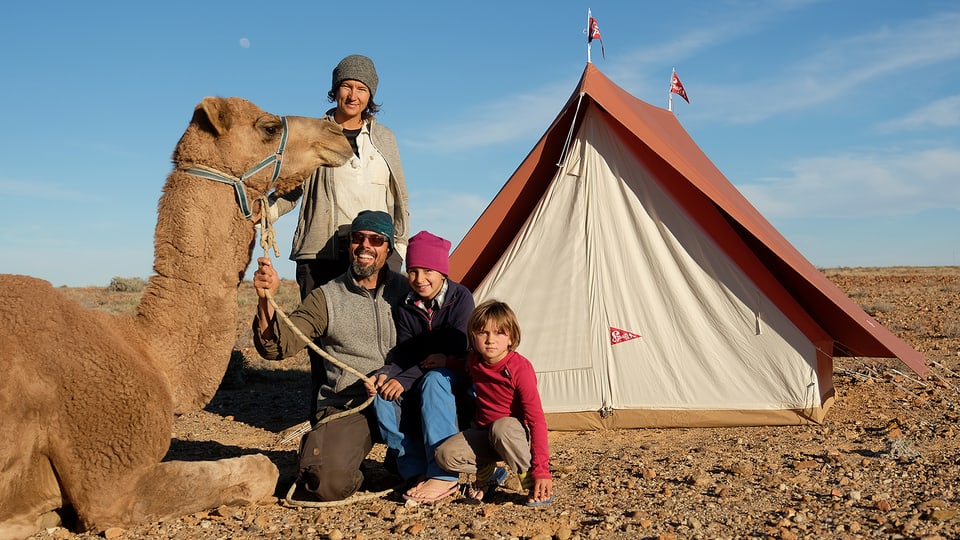 Familie sitzt mit einem Kamel vor einem Zelt.