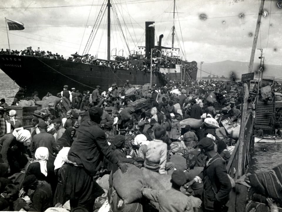 Menschen auf einem überfüllten Quai drängen zu einem Schiff.