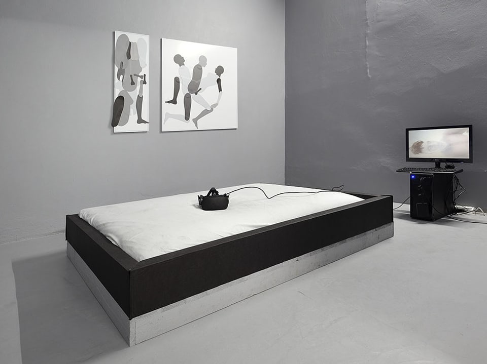 Ein Bett, darauf eine virtual Reality Brille, dahinter ein Bildschirm.