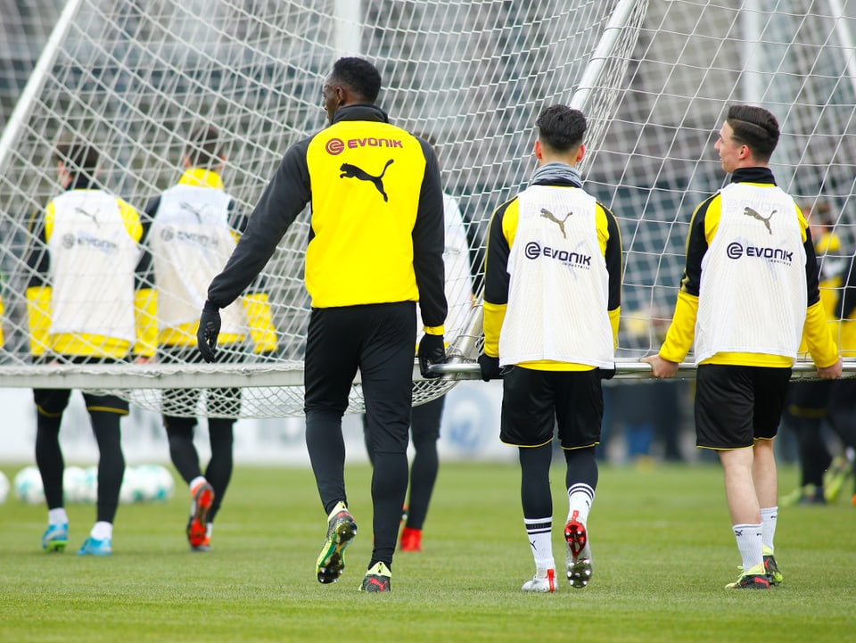 Bolt trägt im BVB-Training zusammen mit anderen Spielern ein Tor.